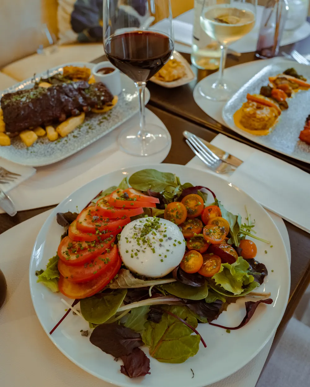 Ensalada de brotes con tomate y queso fresco, con otros platos y copas de vino alrededor