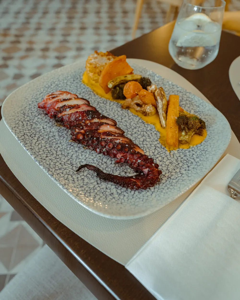 Pulpo a la brasa con parmentier y verduras, servido en una mesa del comedor